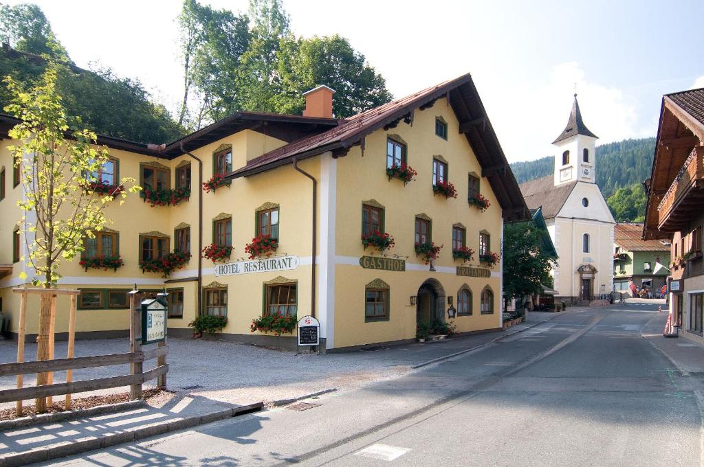 a yellow building with flowers on the windows and a church at Hotel Grafenwirt in Wagrain