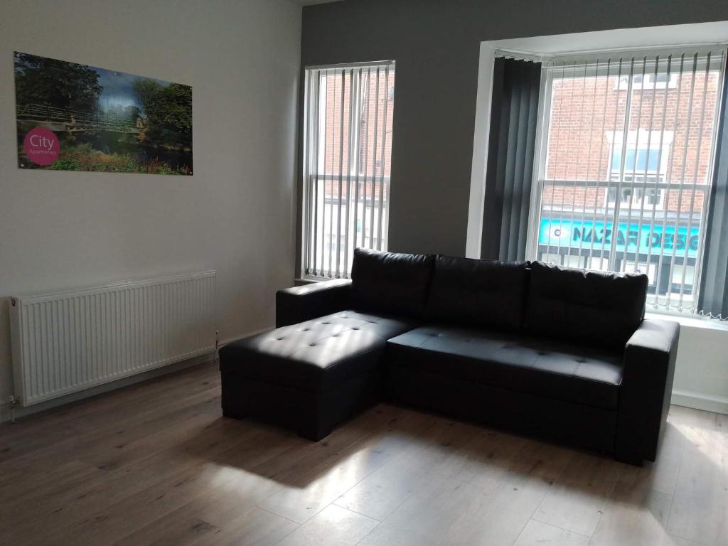 a living room with a black couch and two windows at City Apartments Charles Street in Hull