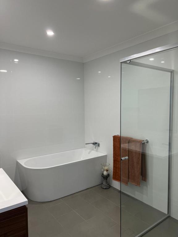 a white bathroom with a tub and a glass shower at Waratah Holiday Home in Unanderra
