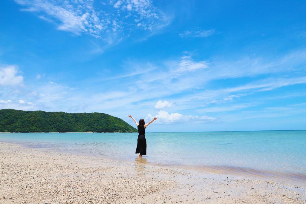 a woman standing on the beach with her arms outstretched at 島の宿　結んちゅ in Amami