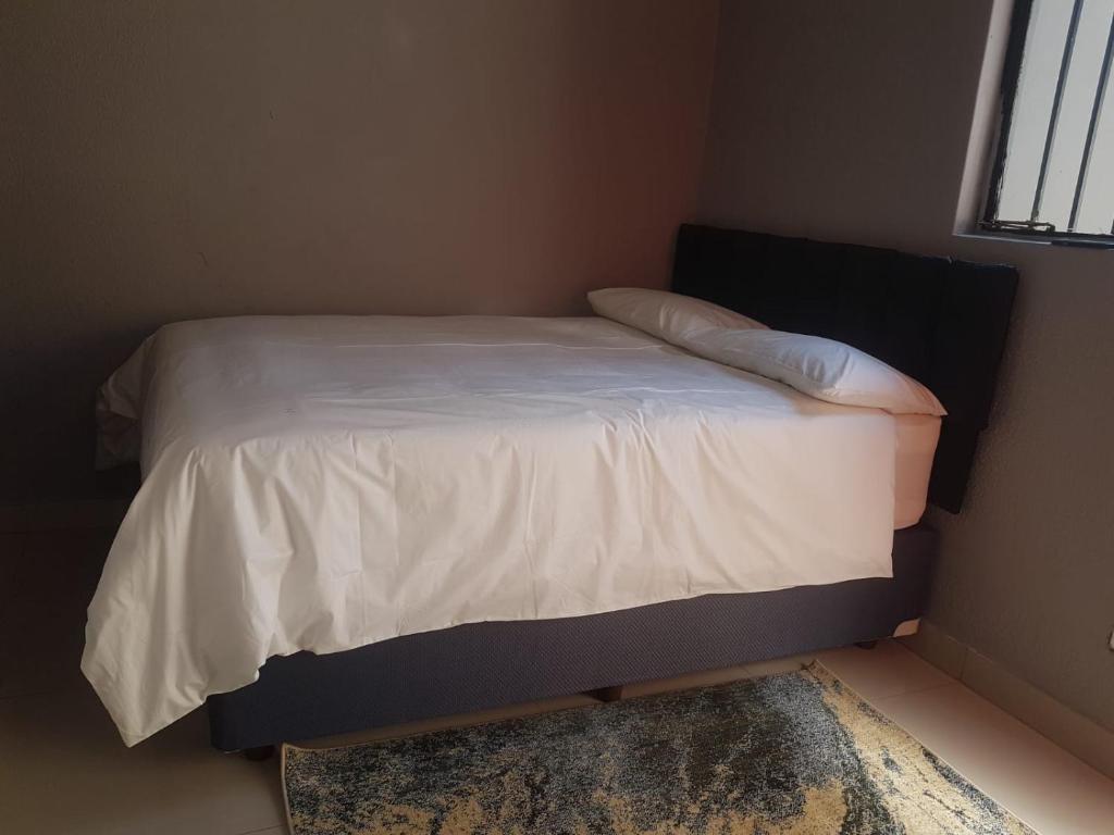 1 dormitorio pequeño con 1 cama con sábanas blancas en Poblar's Bed & Breakfast, en Soweto