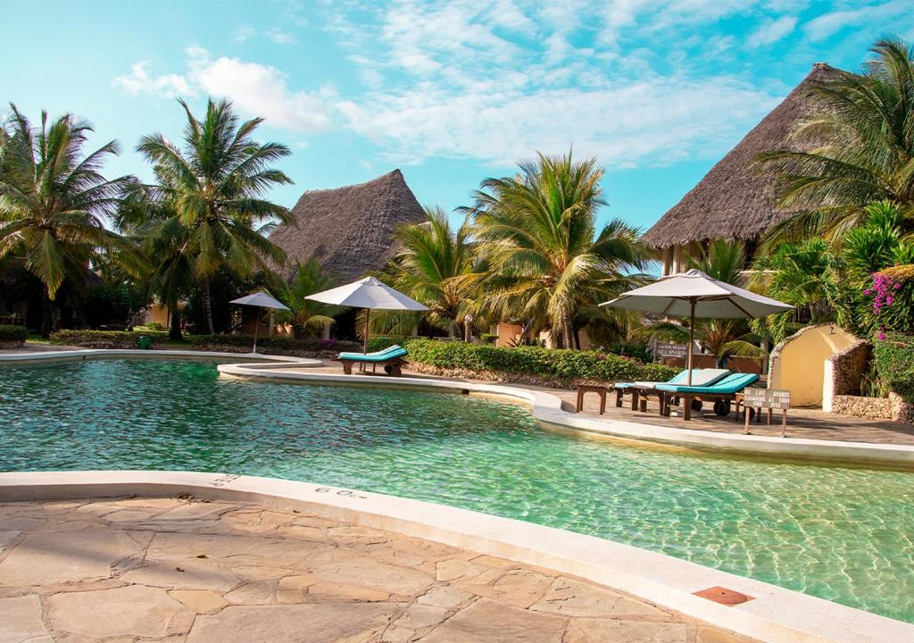 ein Resortpool mit Bänken, Sonnenschirmen und Palmen in der Unterkunft Tembo Court Apartments(Ocean Beach) in Malindi