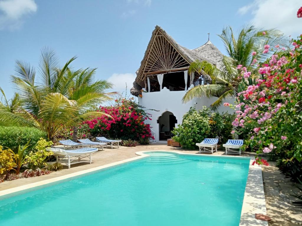 a swimming pool in front of a house with flowers at HUHURU House in Watamu