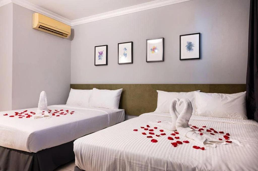 duas camas com pedais de rosas vermelhas num quarto de hotel em # Hashtag Hotel - Self Check in em Alor Setar