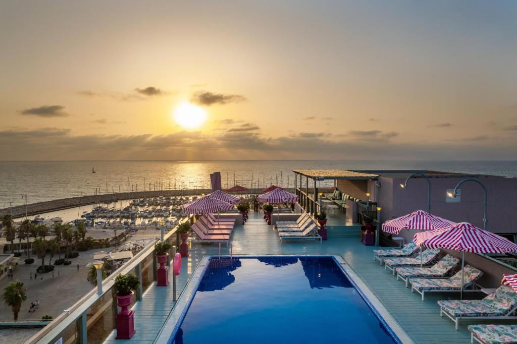 a resort pool with chairs and umbrellas and the ocean at Leonardo Gordon Beach in Tel Aviv