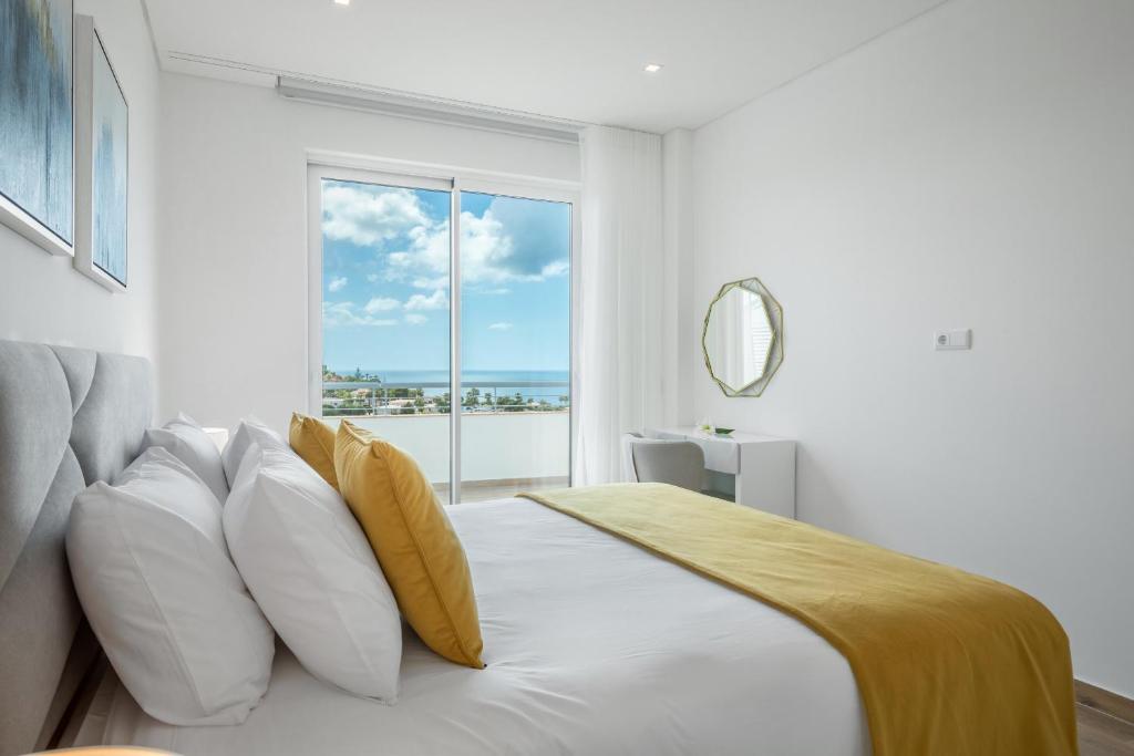 ein weißes Schlafzimmer mit einem Bett mit Kissen und einem Fenster in der Unterkunft Green Beach Ocean View - Porto de Mos in Lagos
