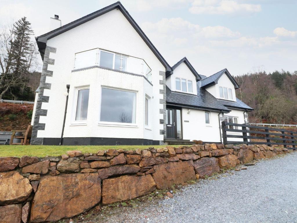a white house with a stone wall at Luxury Highland Home in Scotlands' Great Glen in Gairlochy