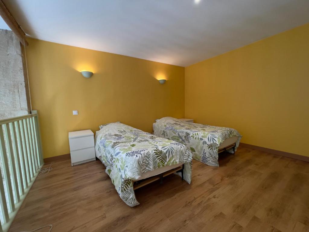 Duas camas num quarto com paredes amarelas e pisos em madeira em La Maison des Pressoirs em Châteauvillain