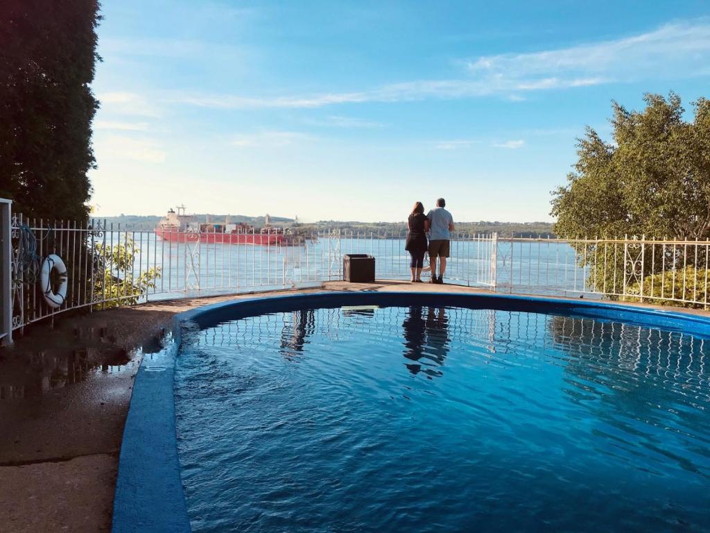 two people standing next to a swimming pool overlooking the water at Goéliche hotel et appartement in Saint-Laurent-de-l'ile d'Orleans