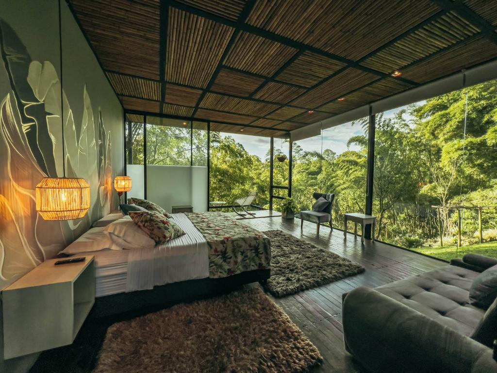 a bedroom with a bed and a living room with windows at Hotel Terra Tacuara in Armenia