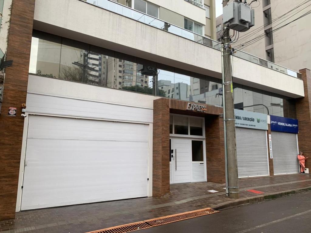 a building with two white garage doors on a street at Novo apto com garagem no centro de Passo Fundo RS in Passo Fundo