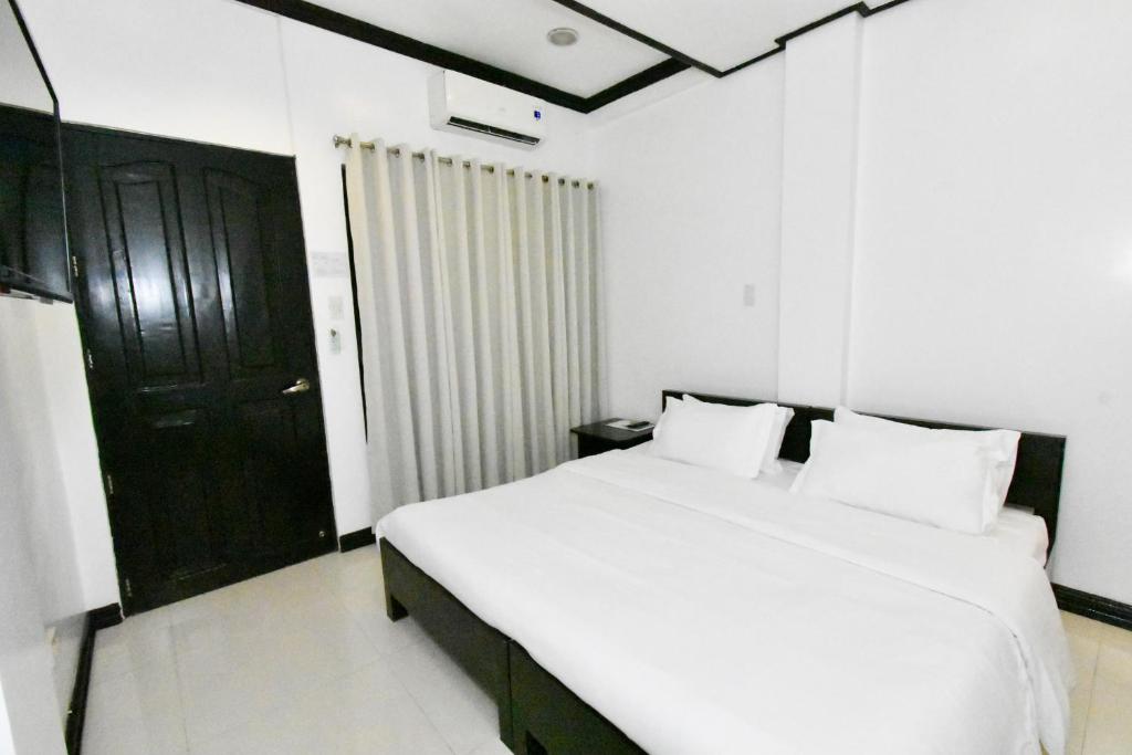 a bedroom with a white bed and a black door at Swiftlets Inn in El Nido