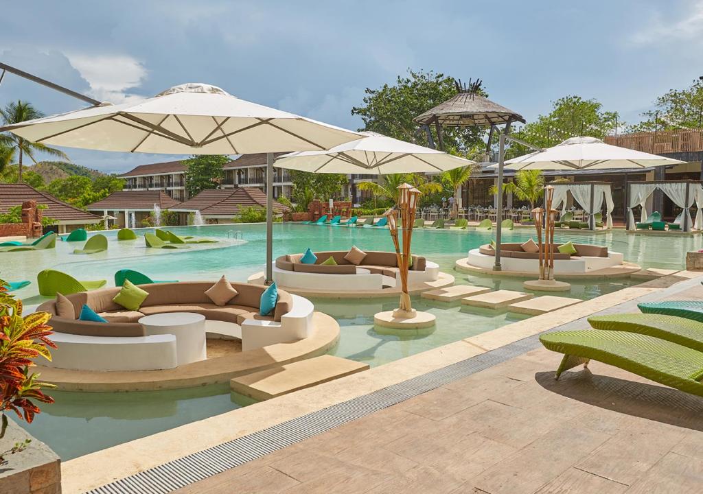 a swimming pool with several couches and umbrellas at Tag Resort in Coron