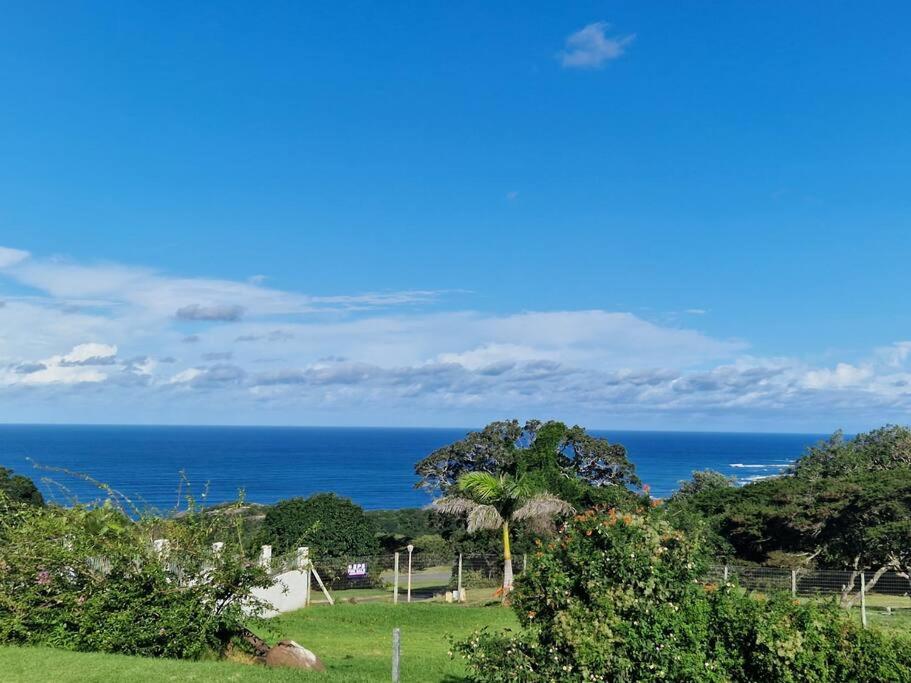 a view of the ocean from a field with trees at HERON COTTAGE - for your seaside holiday. in Chintsa