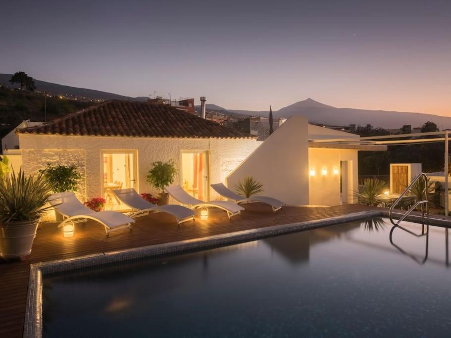 a swimming pool with white chairs and a house at Casa Viña: a spectacular away from it all holiday in La Orotava