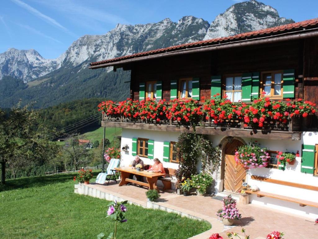 una pareja sentada en un banco frente a una casa con flores en Haus Langbruck Ferienwohnungen, en Ramsau