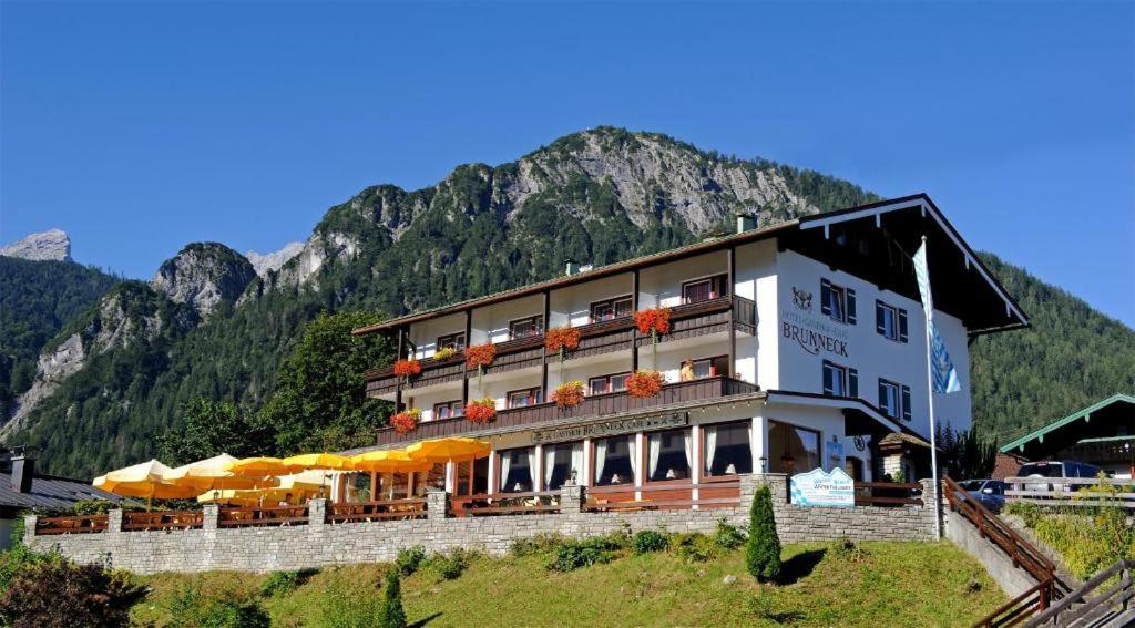 a hotel with tables and umbrellas in front of a mountain at Hotel Brunneck in Schönau am Königssee