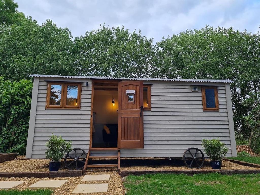 a small white shed with a door and two plants at The Owls Rest Shepherds Hut Hethel in Norwich