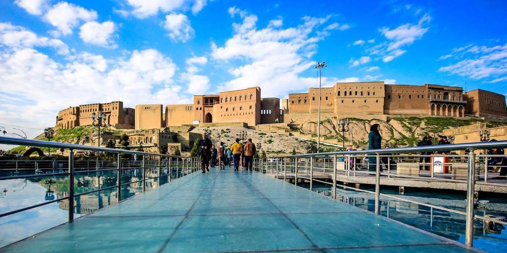 grupa ludzi chodzących po moście przed budynkiem w obiekcie Syros Hotel Erbil City Center w mieście Irbil