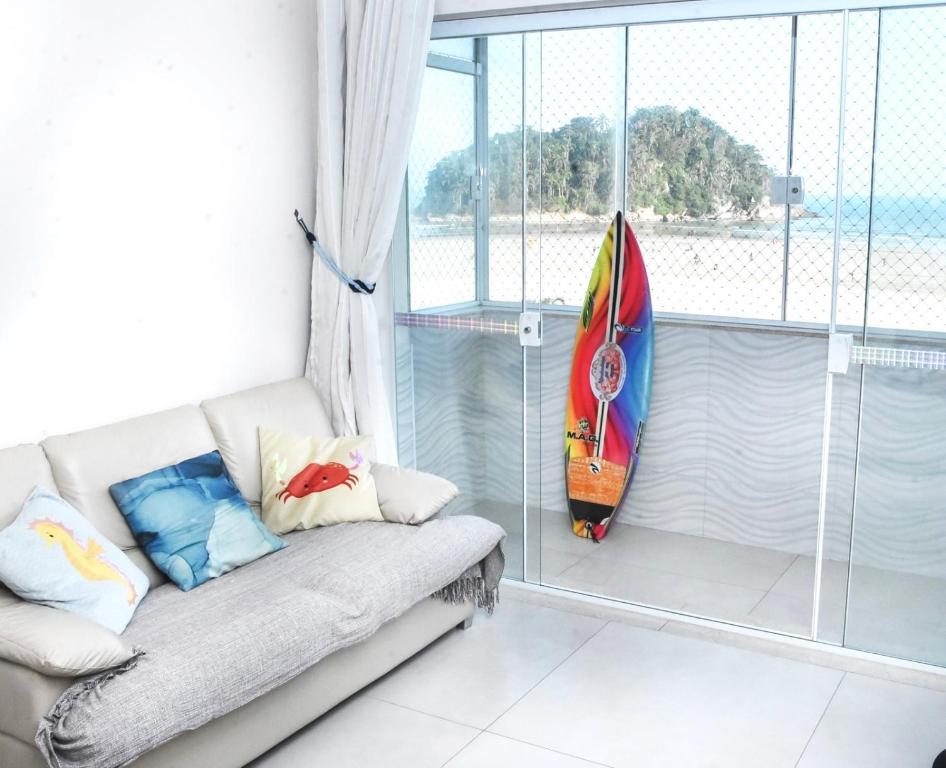a couch in a room with a surfboard leaned against a window at Verdadeiro pé na areia TOP in Santos