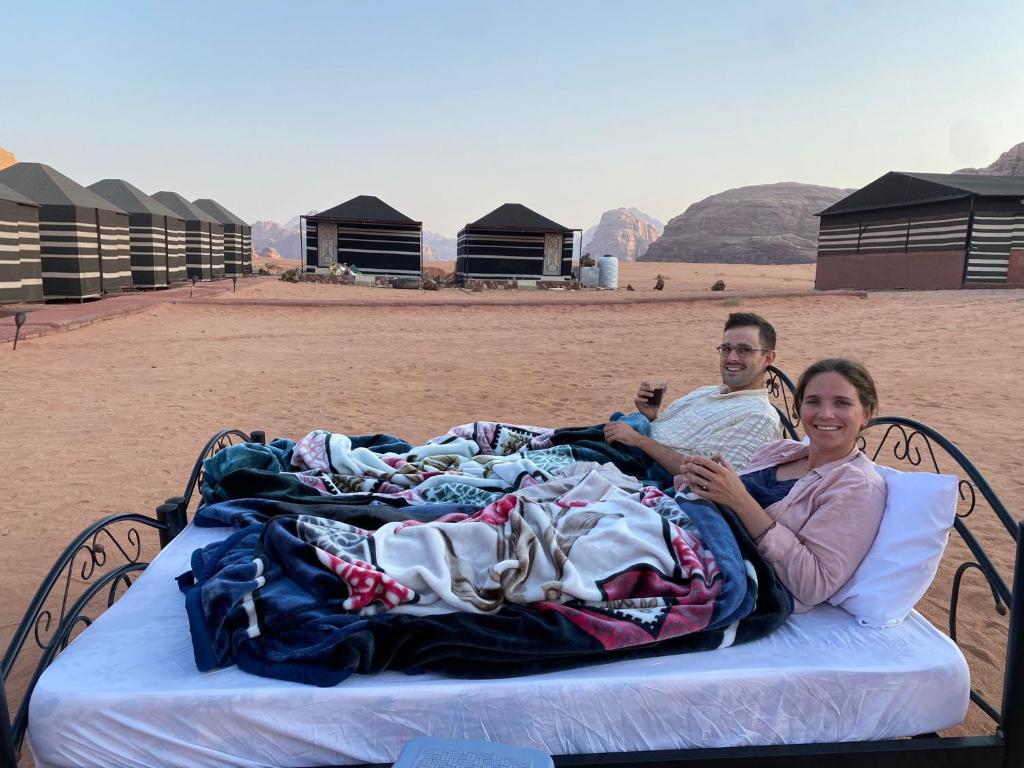 a man and a woman laying on a bed on the beach at Bedouin Tours Camp in Wadi Rum