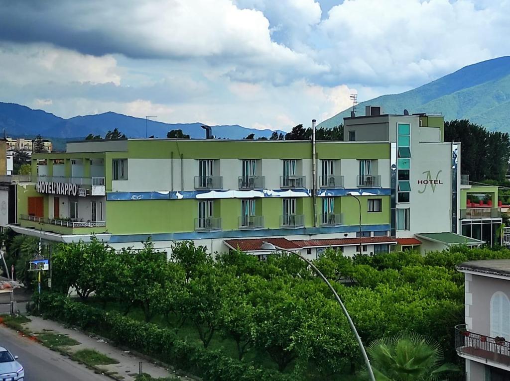 a building with green and white with mountains in the background at Hotel Nappo in San Marzano sul Sarno