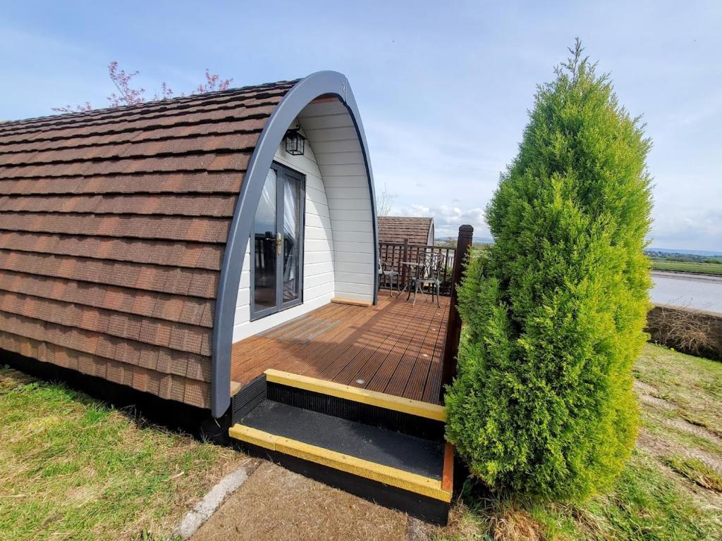 a tiny house with a deck next to a tree at The Golden Ball Luxury Pods in Morecambe