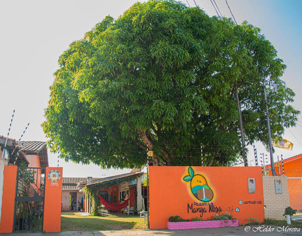 uma parede laranja com uma laranjeira ao lado de uma árvore em Pousada Manga Rosa em Chapada dos Guimarães