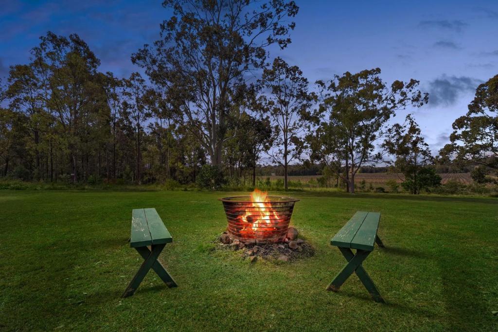 a fire pit in a field with two benches at Glandore Estate Homestead in Pokolbin