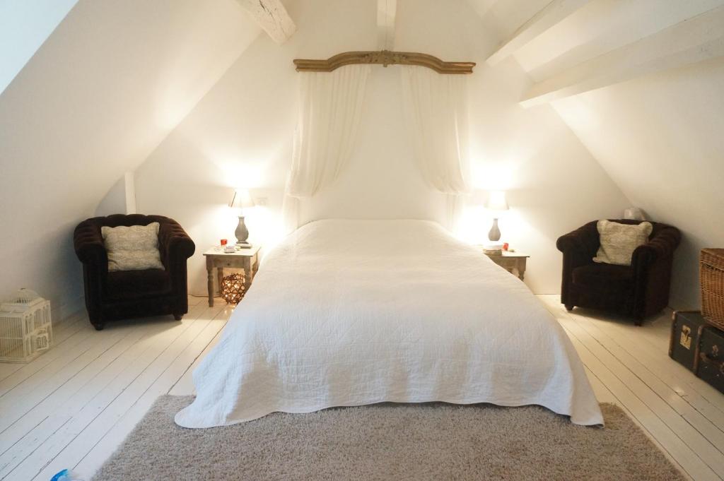 a bedroom with a bed with white sheets and two chairs at La Dépendance in Tours