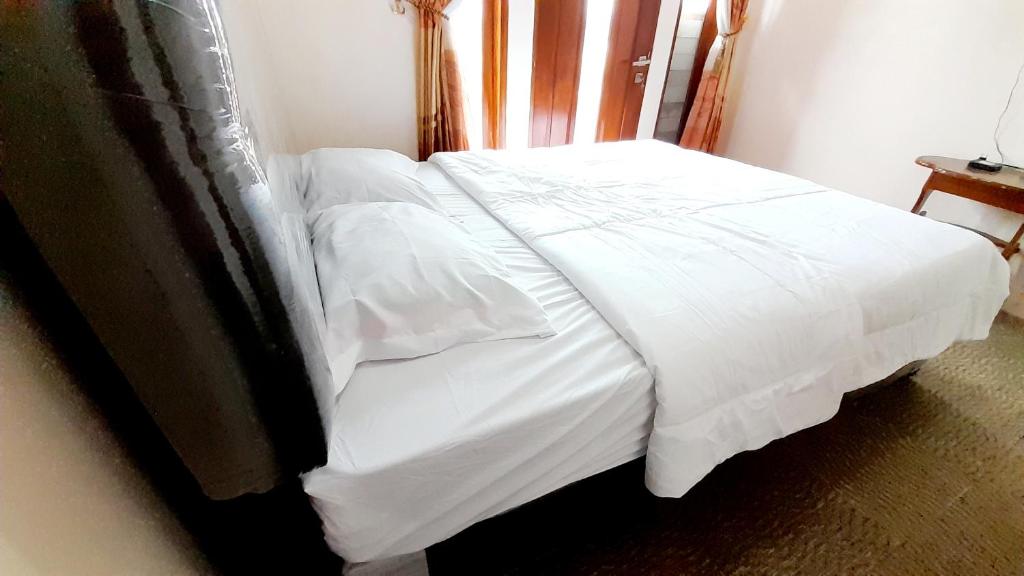 ein Bett mit weißer Bettwäsche und einem Kopfteil aus Holz in der Unterkunft RedDoorz Syariah @ Jalan Pingkan Matindas Manado in Manado