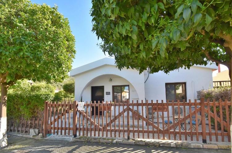 a small white house behind a wooden fence at Bay Cottage Beautiful cosy luxury cottage - Beach area in Pissouri