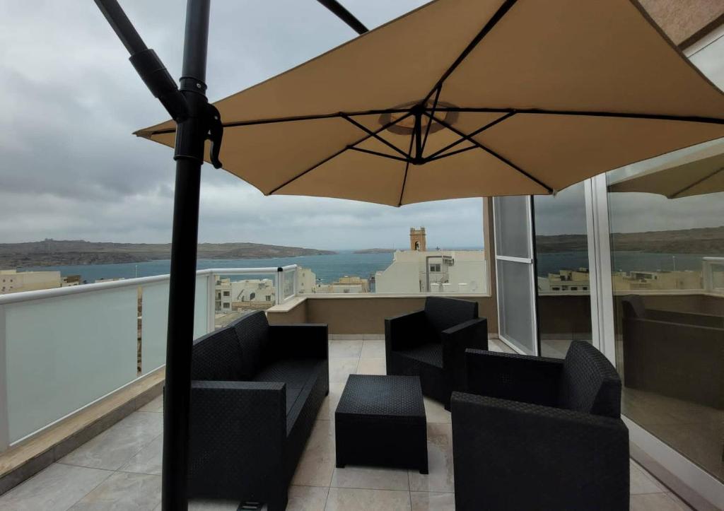 eine Terrasse mit Stühlen und einem Sonnenschirm auf dem Balkon in der Unterkunft ST PAUL'S BAY NEW MODERN PENTHOUSE 2 MINUTES FROM BEACH Seascape Stays in St Paul's Bay