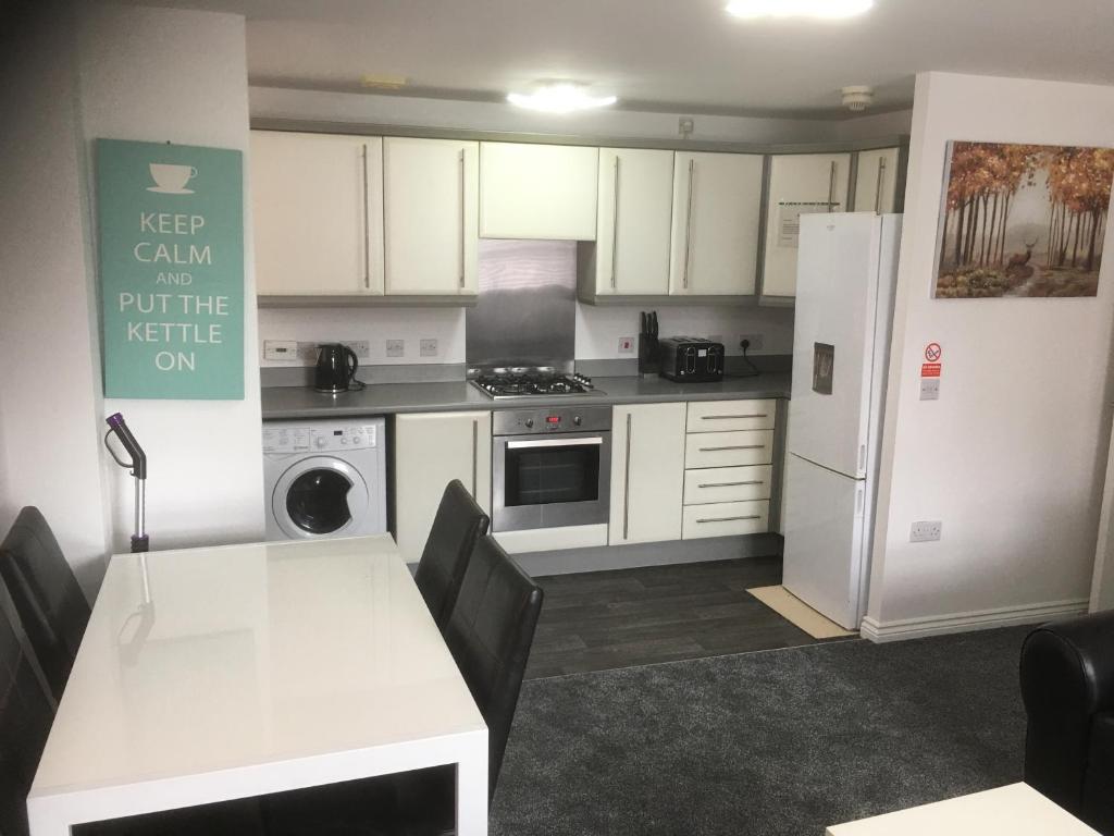 a kitchen with white cabinets and a table and a refrigerator at Beautiful 2 bed apartment with Parking and Wifi and 3 Smart TV's in Great Oakley