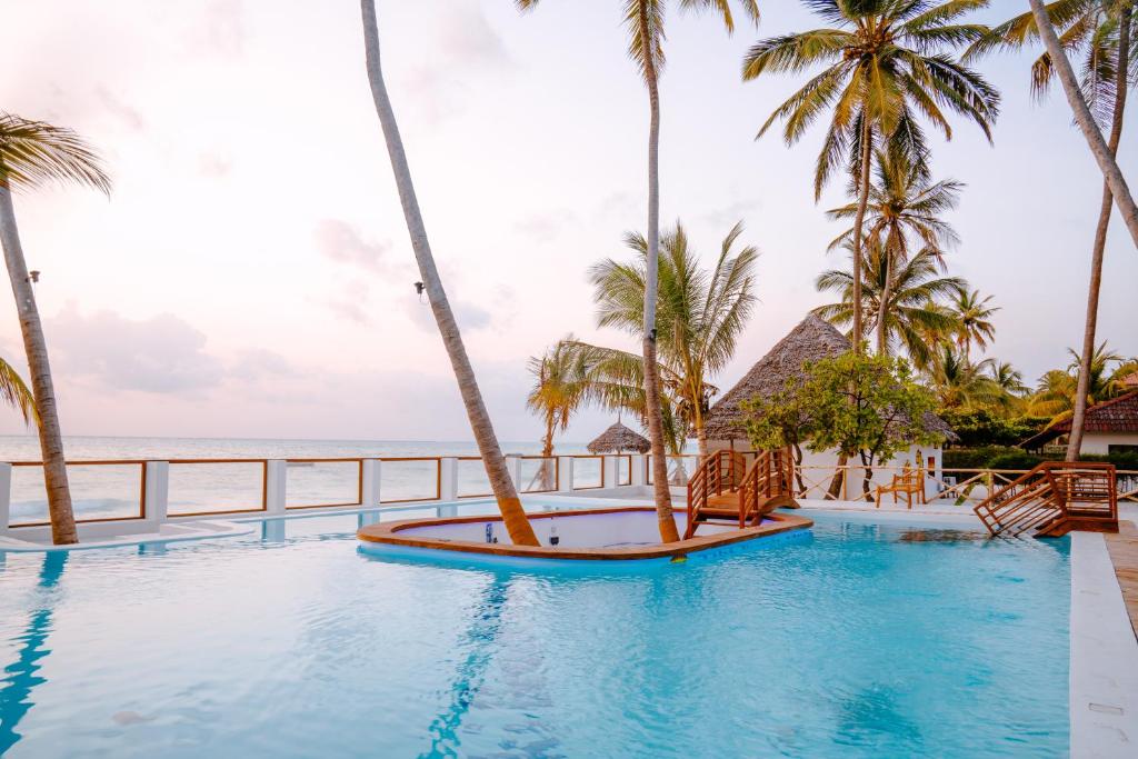 una piscina con palmeras y el océano en TIKI Beach Club & Resort, en Bwejuu