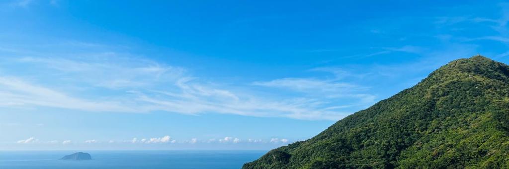 a green mountain with the ocean in the background at Jiufen Breeze 九份惠風民宿ｌ6人包棟小屋 in Jiufen