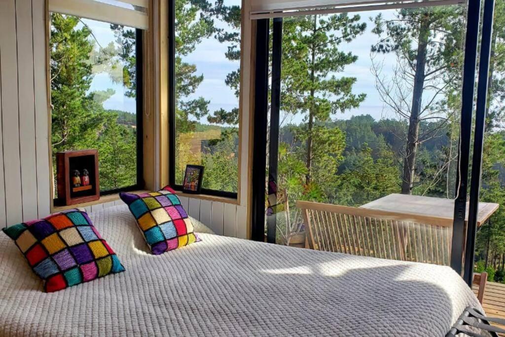 - une chambre avec un lit en face d'une grande fenêtre dans l'établissement Tinyhouse Boyeruca Lodge. Maravillosas vistas de Bosque, Mar y Cielo, à Vichuquén