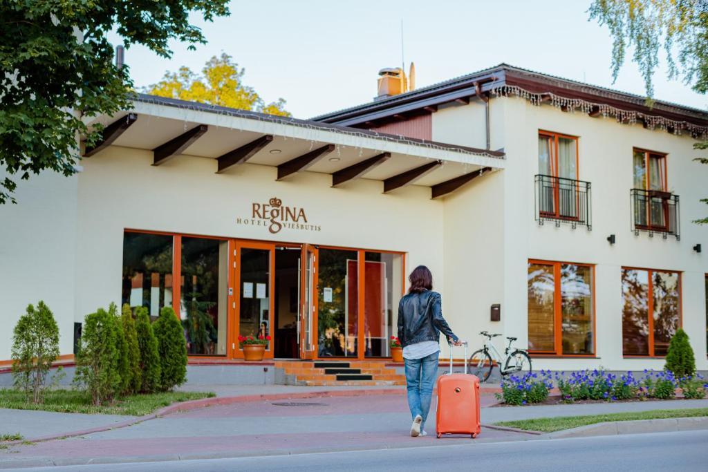 a woman walking in front of a building with a suitcase at Regina in Druskininkai