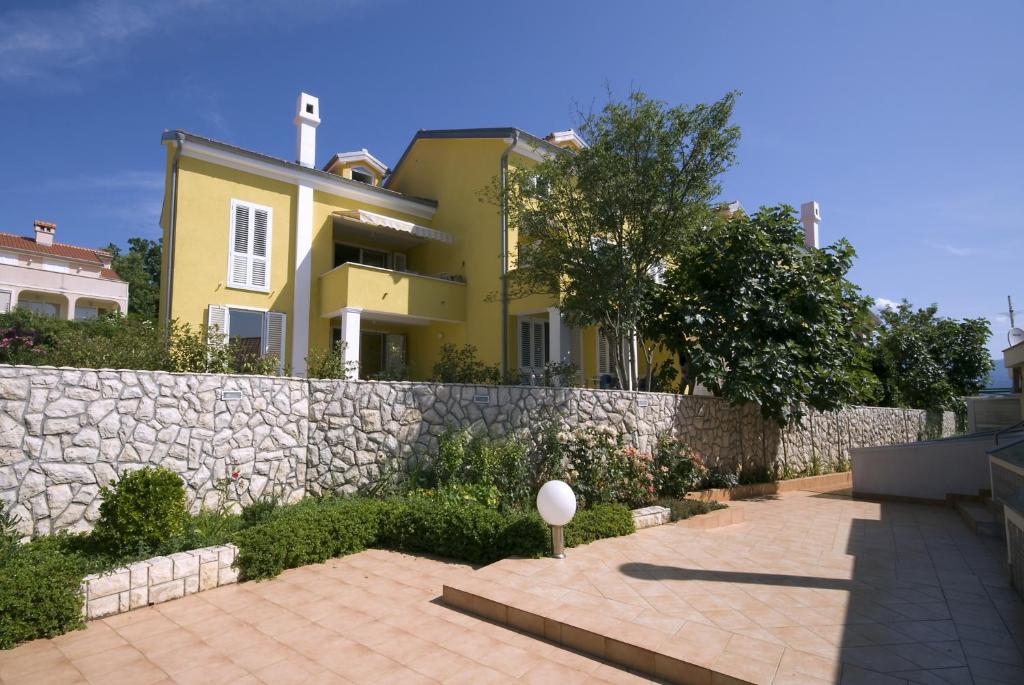 een geel huis met een stenen muur en een hek bij Apartments by the sea Cizici, Krk - 15496 in Malinska