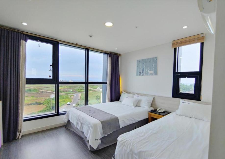 済州市にあるSky Hotelのベッド2台と大きな窓が備わるホテルルームです。