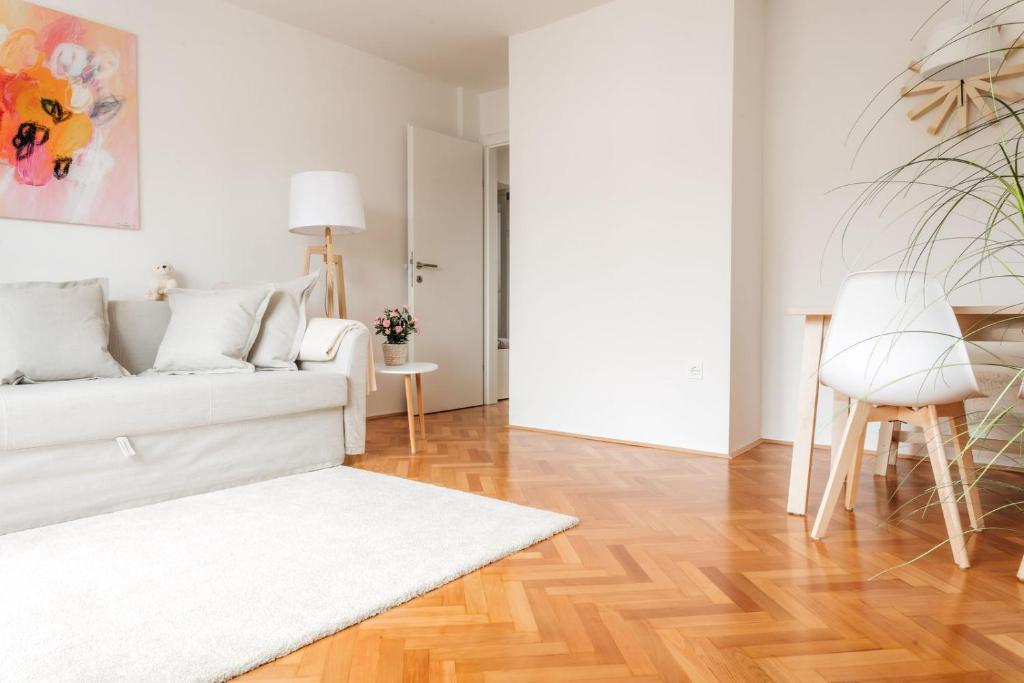 a living room with a white couch and a wooden floor at White Apartment in Ljubljana