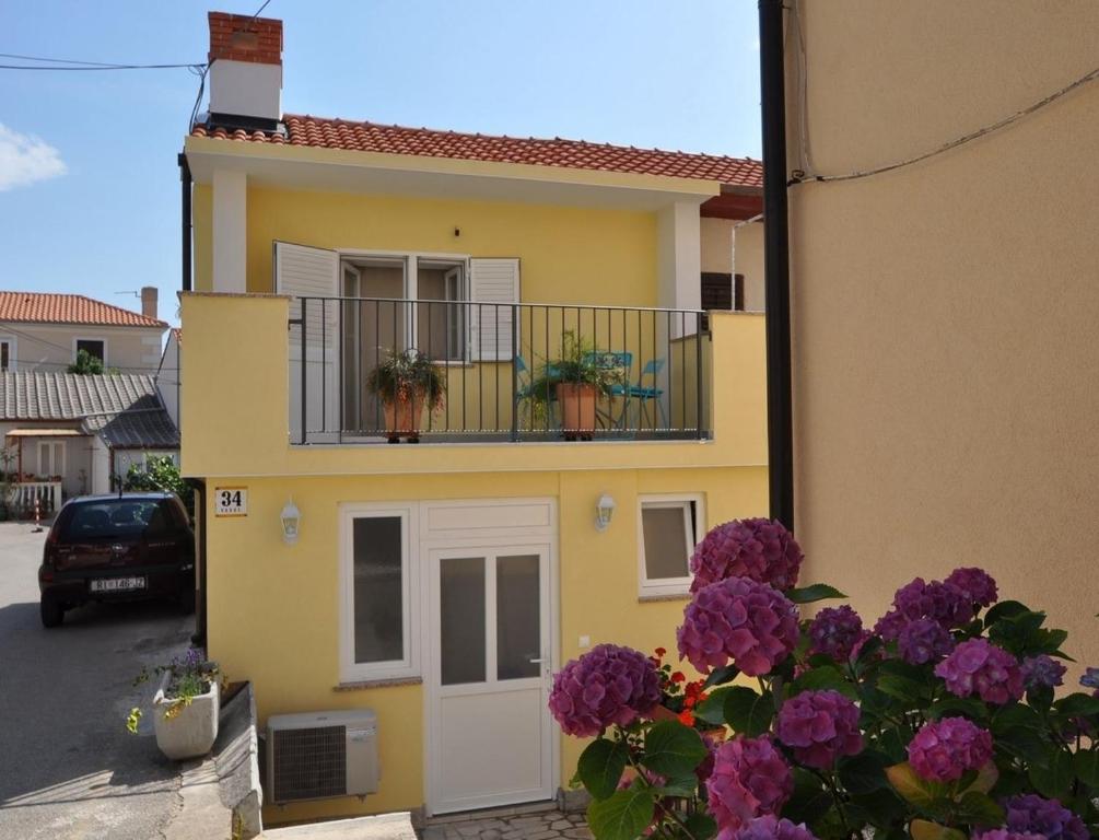 a yellow house with purple flowers on a balcony at Apartments by the sea Vrbnik, Krk - 15754 in Vrbnik