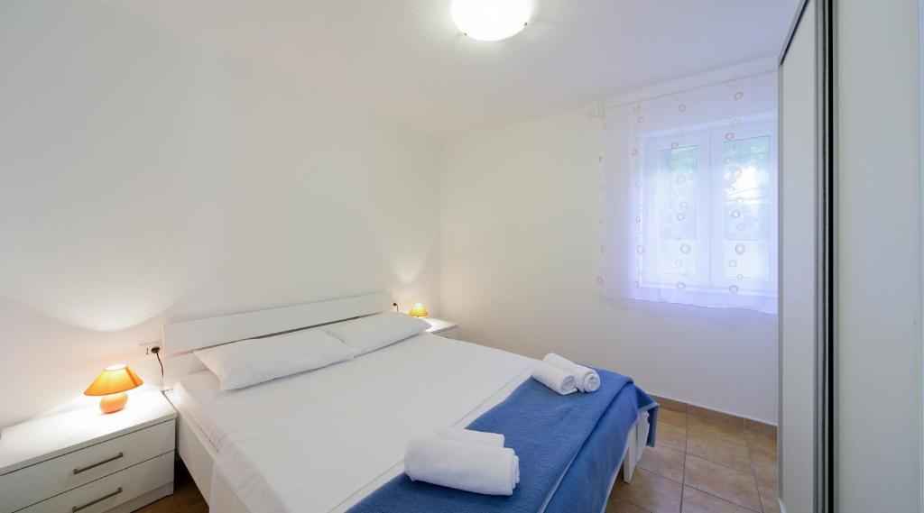 a white bedroom with a bed and a window at Apartments by the sea Nerezine, Losinj - 15778 in Nerezine