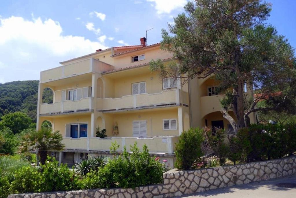 a large yellow building with a tree in front of it at Apartment Supetarska Draga - Donja 15983c in Rab