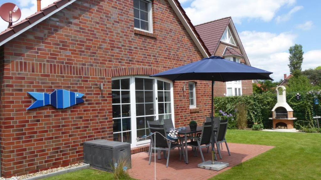 - une table et des chaises avec un parasol en face d'une maison dans l'établissement An den Zwillingsmühlen, à Greetsiel