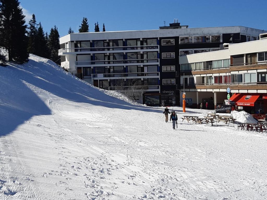 dos personas esquiando por una pista cubierta de nieve frente a un edificio en Studio aux pieds des pistes Roche Béranger, en Chamrousse