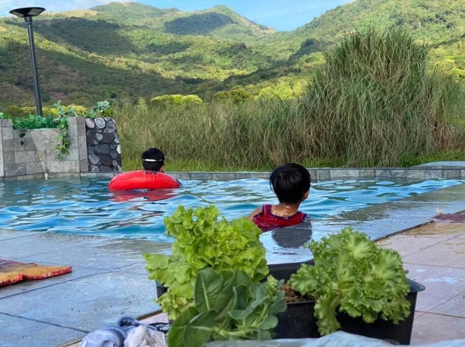 two children in a swimming pool with mountains in the background at Casita Blanca Jala-Jala - Tiny House & Farm Stay in Jalajala