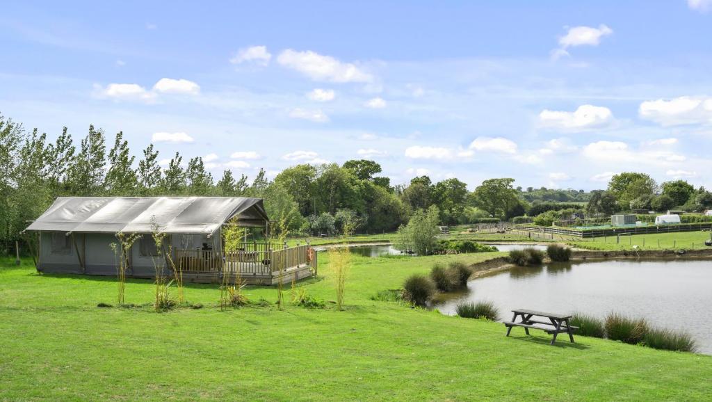 un bâtiment dans l'herbe à côté d'un lac dans l'établissement Finest Retreats - The Herdwick Safari Tent, à Hertford