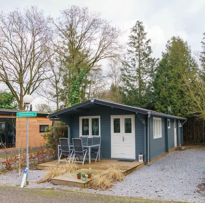 een klein huis met een veranda en stoelen op een patio bij Gezellig ingerichte blokhut op een rustig park! in Putten