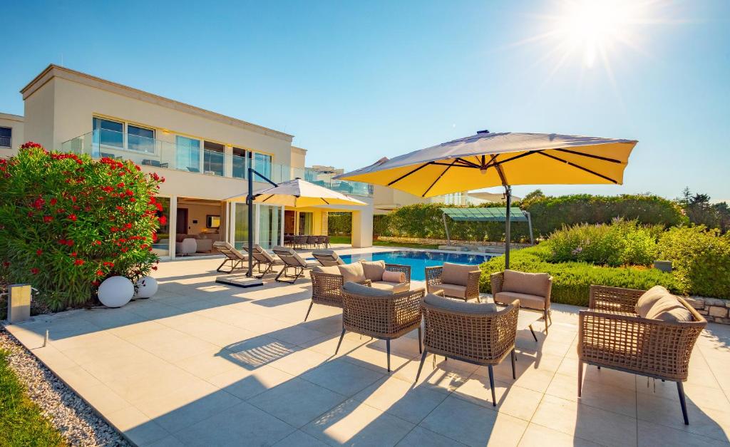 a patio with chairs and an umbrella and a pool at Lusso Mare Istria Luxury Beach villa in Savudrija